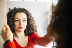 Woman,with,curly,hair,standing,in,front,of,large,mirror 